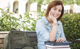 Smiling Young Pretty Female Student Sitting Outside on Bench with Backpack, Books and Touch Tablet.